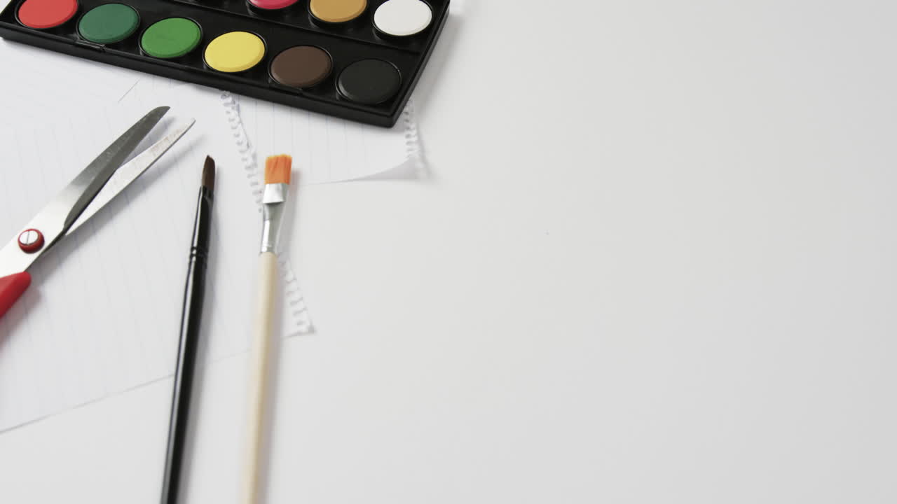 Close up of paints, brushes and scissors on white background with copy space, in slow motion