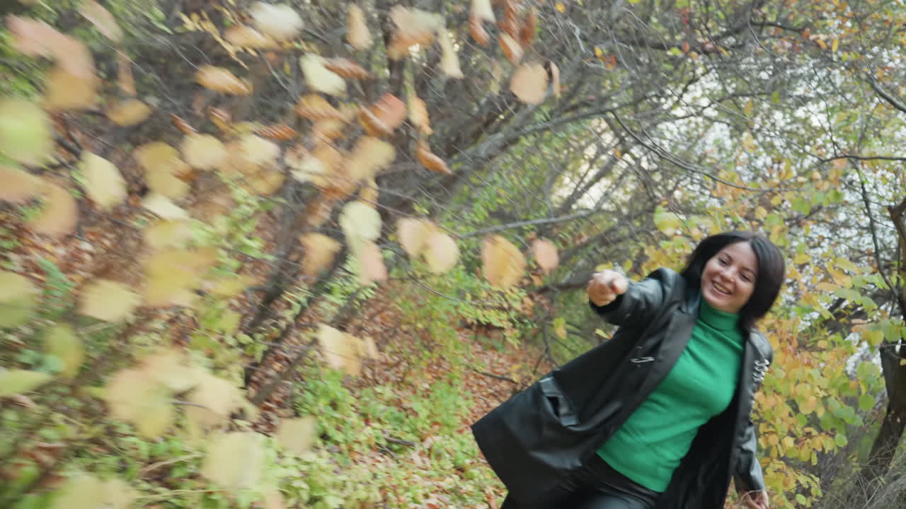 Woman in leather jacket runs through woods, Quick woman pushes ahead amidst fallen leaves in forest, Woman swiftly advances through forest terrain covered with colorful autumn foliage