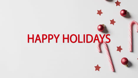 happy holidays text in red with candy canes, red stars and christmas baubles on white background