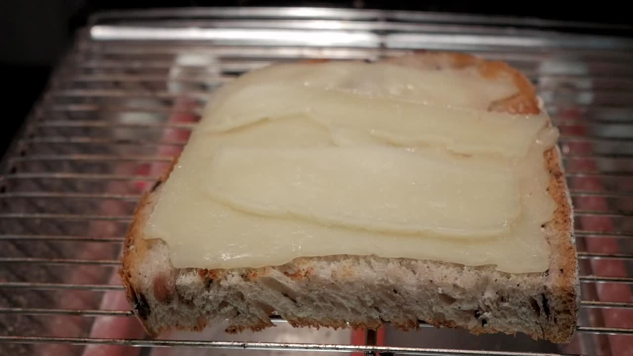 A piece of toast topped with melted cheese, placed on a wire rack for further toasting