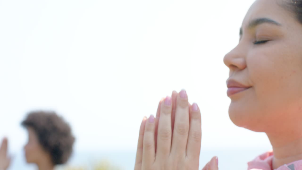 Donne con felpa rosa e top blu che alzano le braccia, uniscono i palmi delle mani e si allungano in riva all'oceano, spazio per il testo