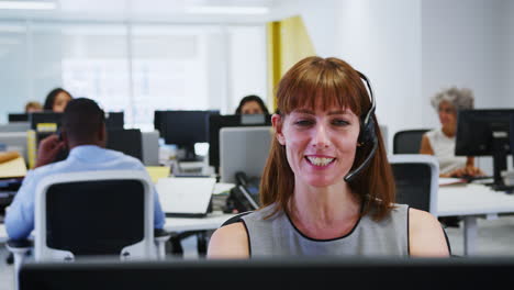 Young-woman-working-at-computer-with-headset-in-busy-office