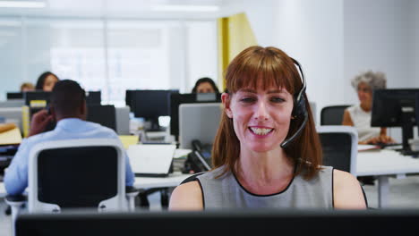 young woman working at computer with headset in busy office