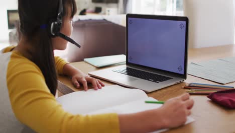 Asian-girl-at-home-wearing-headset-during-online-school-lesson-using-laptop,-copy-space-on-screen