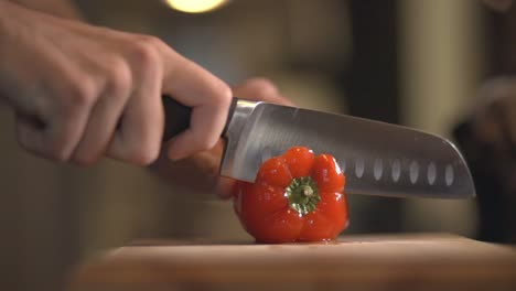 chef's hand slicing a red sweet bell pepper to remove the seeds