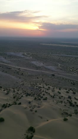 an aerial top view of golden sand dunes in jaisalmer, rajasthan, dotted with patches of green vegetation with the dramatic sky rajasthan india 4k drone