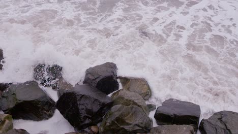 Slow-motion-close-up-view-looking-down-at-sea-crashing-onto-rocks-on-a-dull-day,-Whitby-North-Yorkshire-England-UK