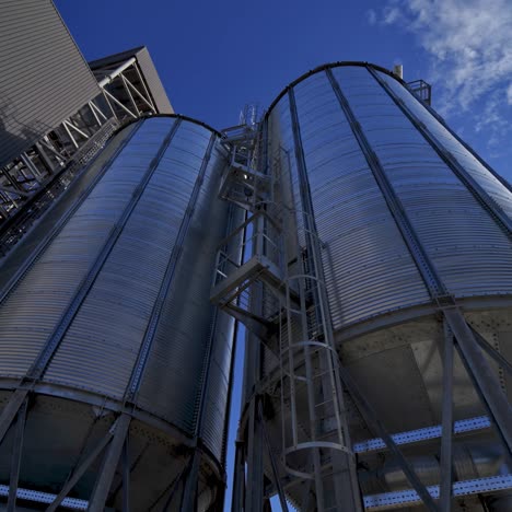 silver containers outside. modern agricultural complex against blue sky. large grain elevators. industrial plant. view from below.
