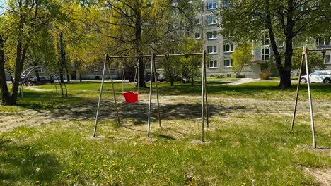 An-abandoned-red-children's-swing-swings-with-the-wind-in-summer-in-a-soviet-courtyard