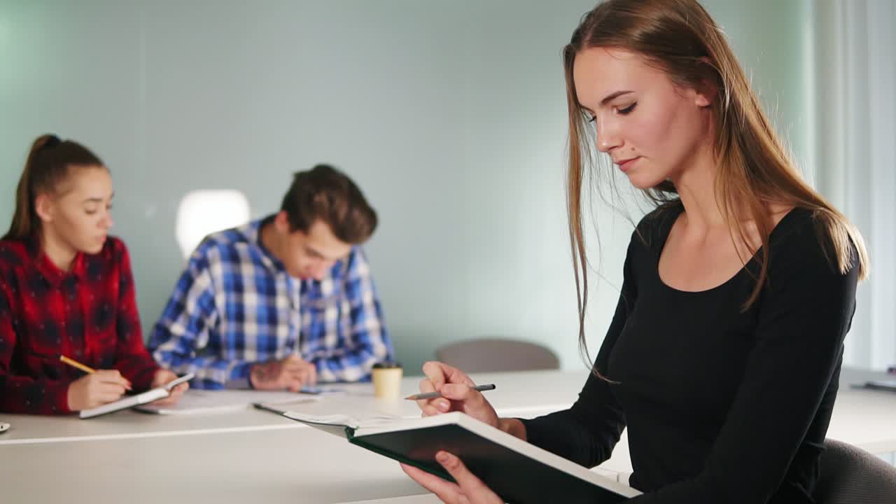 retrato de una joven estudiante leyendo un libro y trabajando en su tarea mientras sus amigos están estudiando en el fondo