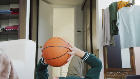 asian boy playing with basketball lying on the floor at home