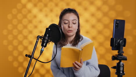 Narrator-looking-at-phone-camera,-filming-herself-reading-book-for-kids