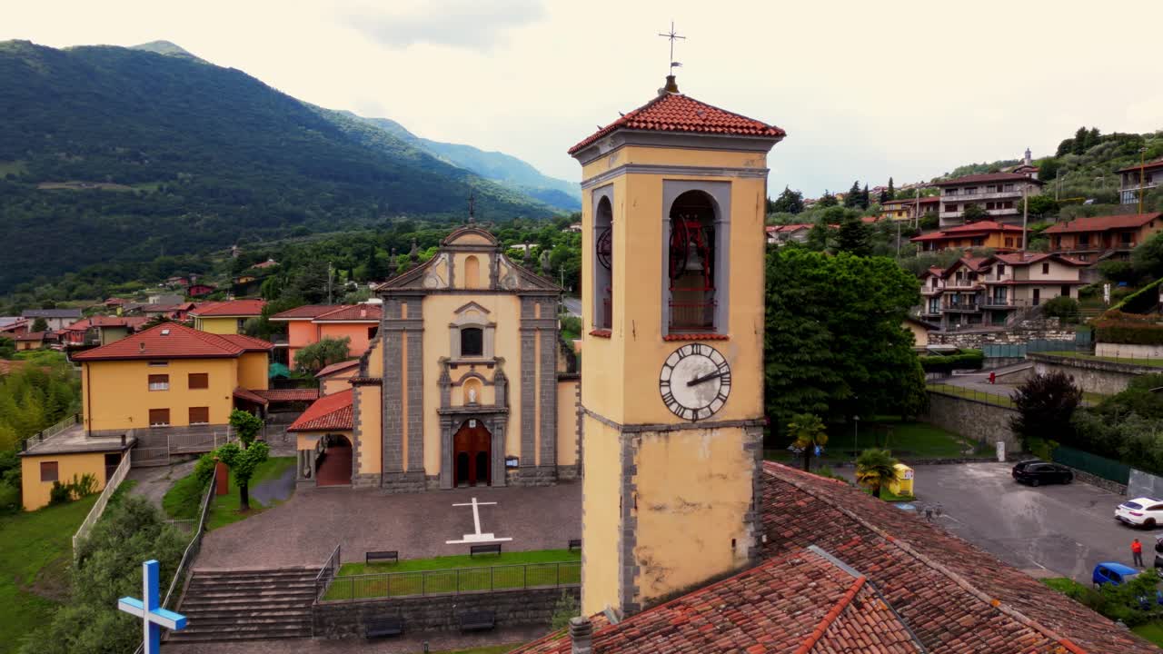 Detail view of the yellow bell tower in Riva di Solto, with backdrop of hills and rooftops. Riva di Solto, Bergamo, Italy (Riva di Solto, Bergamo, Italia)
