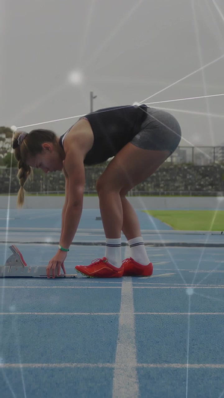 Atleta feminina ajustando os blocos de partida na raia azul da pista, usando sapatilhas vermelhas