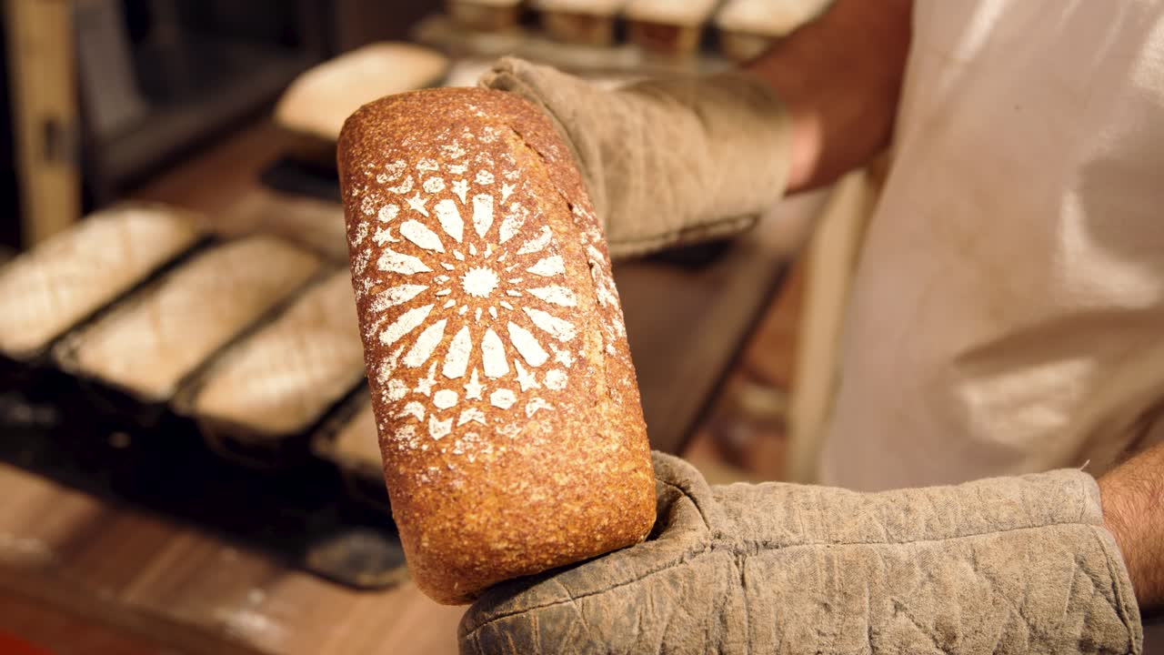 Padeiro segurando um pão artesanal recém-assado com luvas de forno