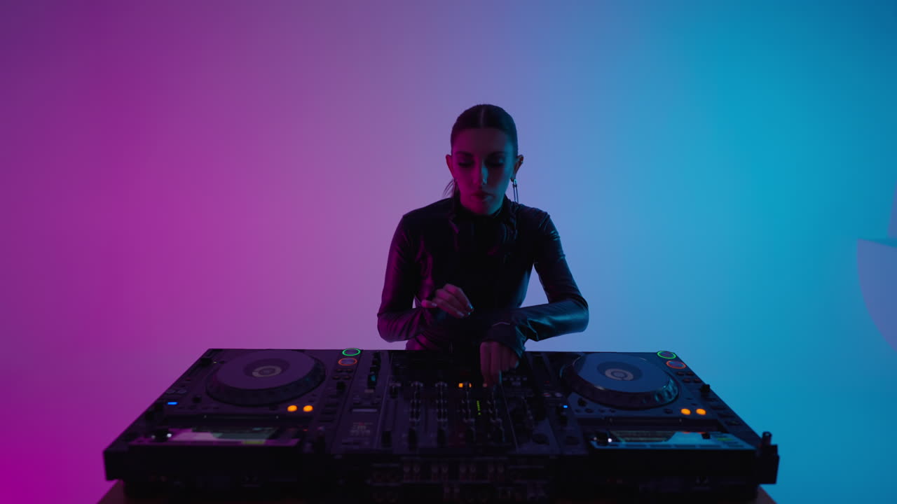 A female DJ mixing music on a set of turntables in a studio.