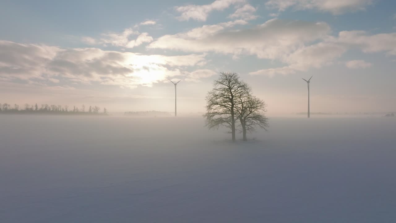 풍력 발전소에서 재생 가능한 에너지를 생성하는 풍력 터빈의 공중 전망, 안개로 가득 찬 눈으로 가득 찬 시골 풍경, 황금 시간의 빛이 있는 화창한 겨울 저녁, 넓은 추적 드론 샷이 왼쪽으로 이동