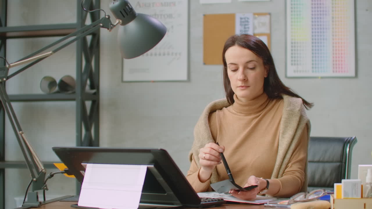 A young designer girl draws on a modern graphic screen using a workstation in an office with large Windows. Create logo design and graphics