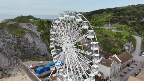 drone capturing ferris wheel moving beside rocky mountains in england, uk. the towering peaks contrast with lively scene, creating unique blend of natural and recreational scenery