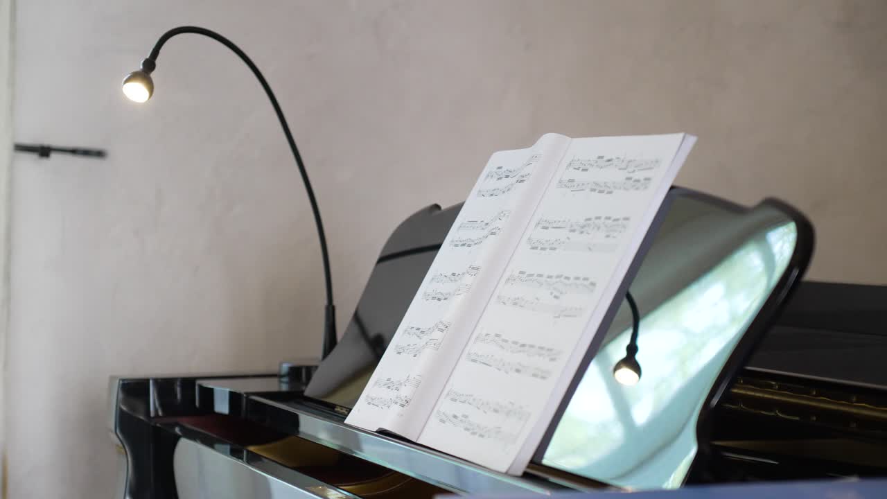 disparo en órbita lenta que muestra la partitura dejada abierta sentada en la parte superior de un piano negro brillante