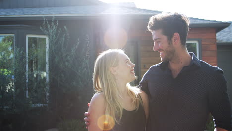 portrait of hugging couple standing outdoors in front of house against flaring sun