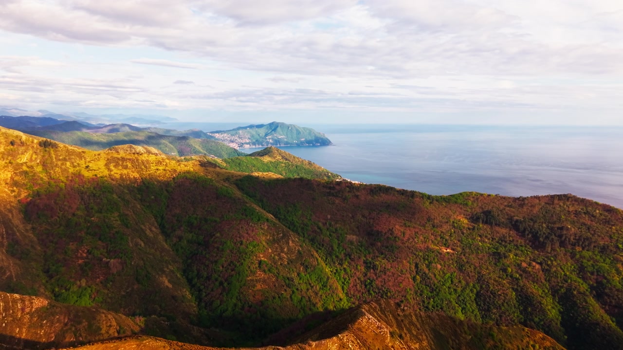 En spektakulær luftig droneutsikt over en ulendt fjellkjede som stuper direkte ned i havet i Liguria, Italia, vakkert belyst av kveldens gylne time.