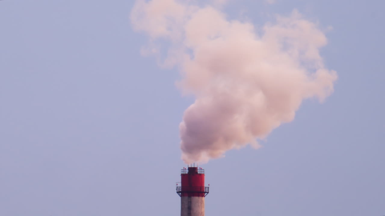 Ciminiera industriale che rilascia fumo denso nel cielo sopra un cantiere edile cittadino.
