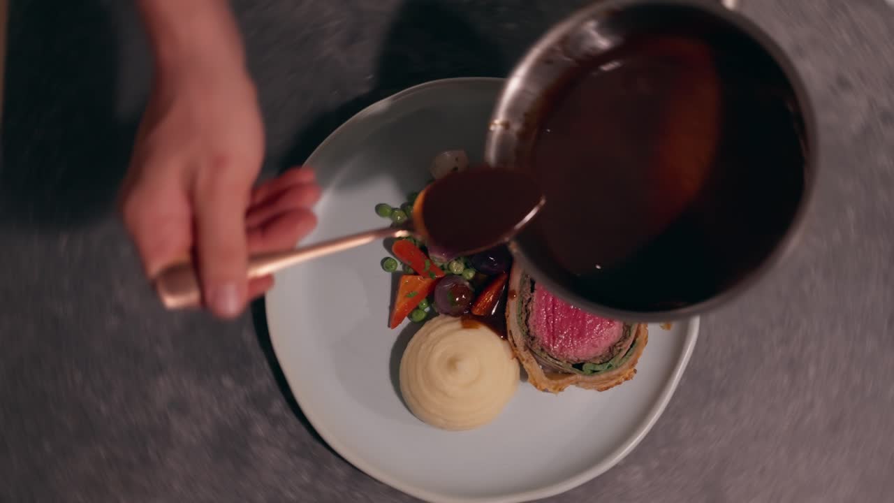 Akşam yemeği servisi için hazırlanan ve soslanan, Beef Wellington, sebzeler ve patates püresinden oluşan canlı bir yemek (ağır çekim 4K).