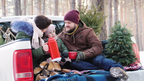 a young family of three people is drinking hot tea from a thermos sitting in the back of a car near