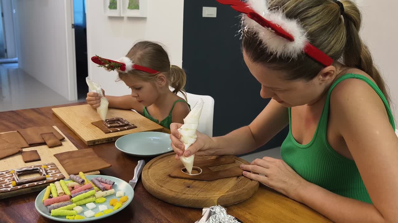 madre e hija decorando una casa de pan de jengibre para navidad
