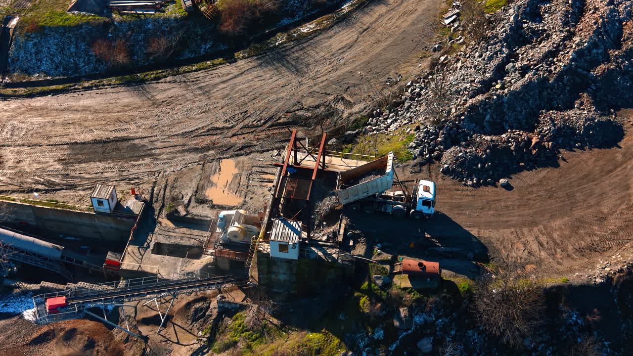 Truck unloading raw stones into industrial crusher at quarry. High angle shot of a white dumper truck tipping granite rocks into a heavy duty crushing machine