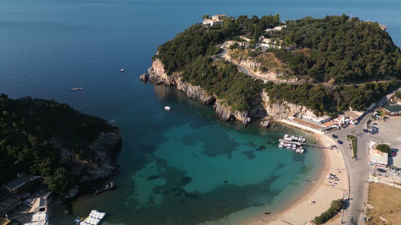 estabilización aérea en órbita sobre la playa de arena dorada y la cala en corfú, grecia, con barcos en el muelle y turistas en la playa