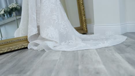 a drop down shot of a white wedding dress hanging on a mirror prior to a wedding