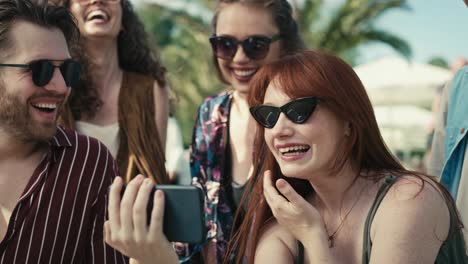 Gruppe-Kaukasischer-Freunde-Auf-Einem-Musikfestival,-Die-Lustige-Fotos-Durchstöbern,-Die-Gerade-Mit-Einem-Mobiltelefon-Aufgenommen-Wurden.