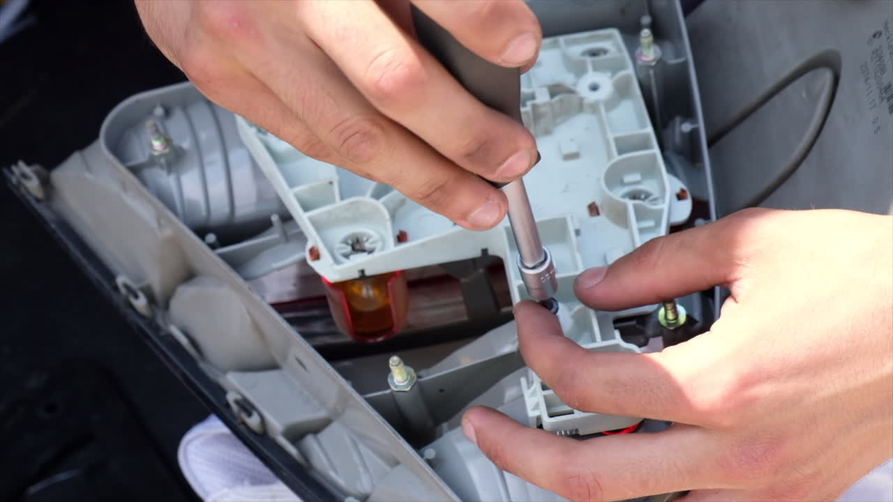 Close up of a man using a screwdriver to work on the headlight of a car