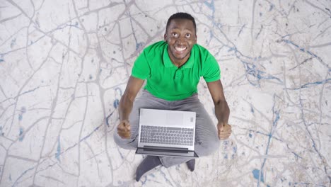 un joven negro feliz y positivo usando una computadora portátil y regocijándose. regocijándose con pasión.