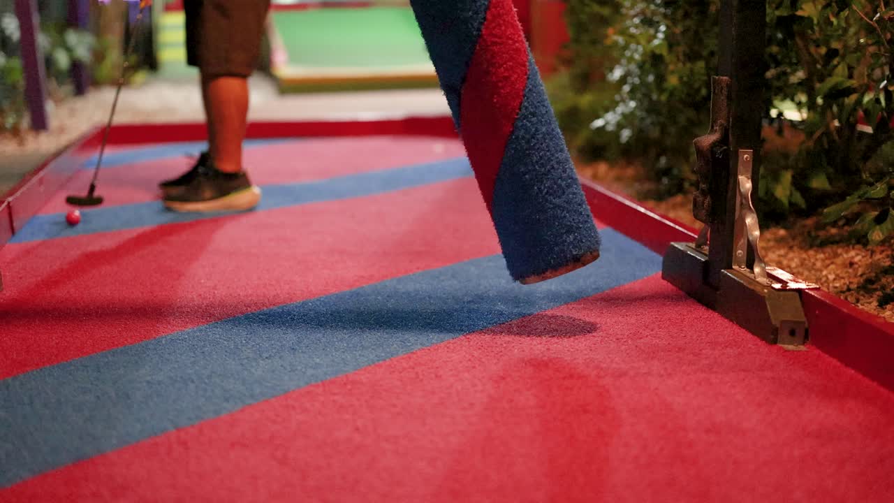 A golfer putts a ball through a rotating obstacle on a colorful mini-golf course at night