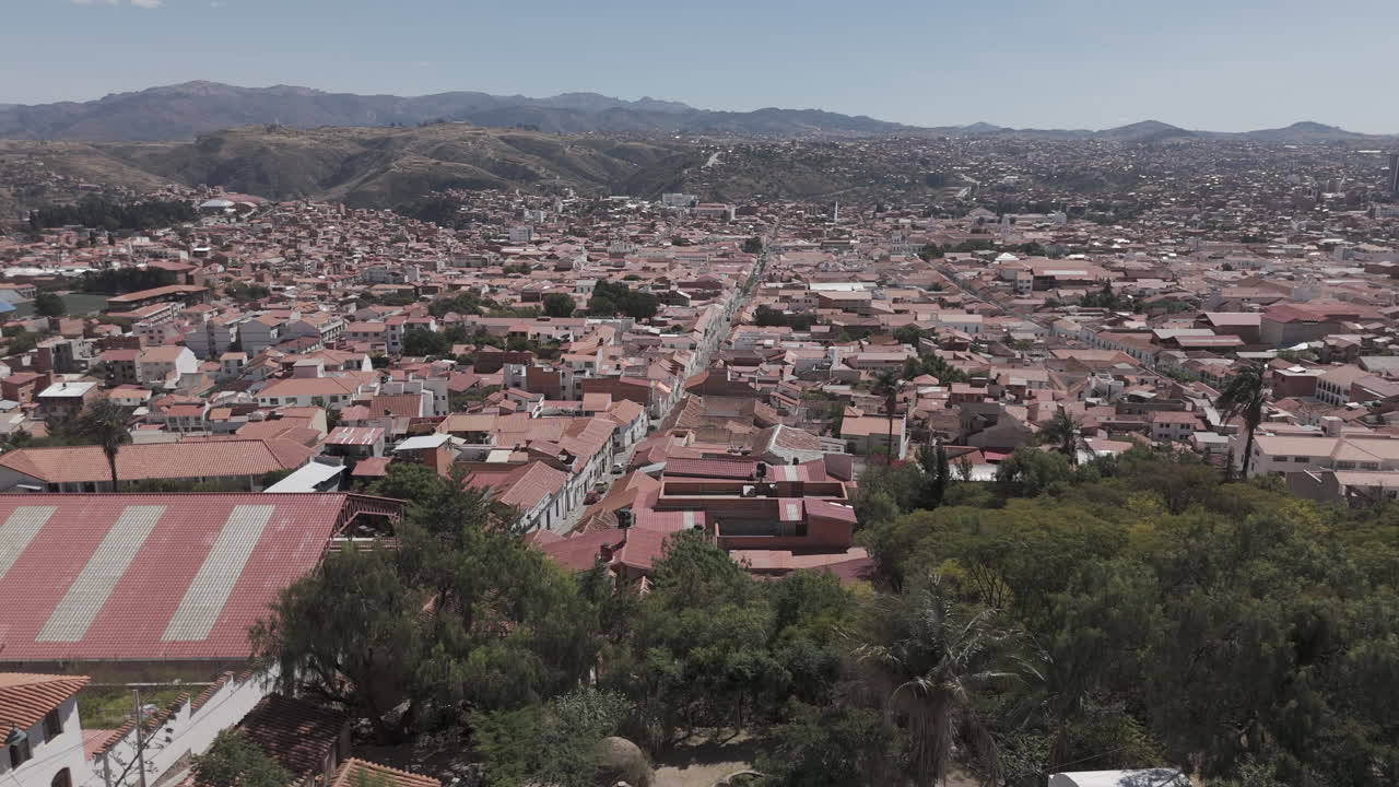 Wide drone shot of Sucre Bolivia on a bright day with blue sky from behind the square on top of the city LOG