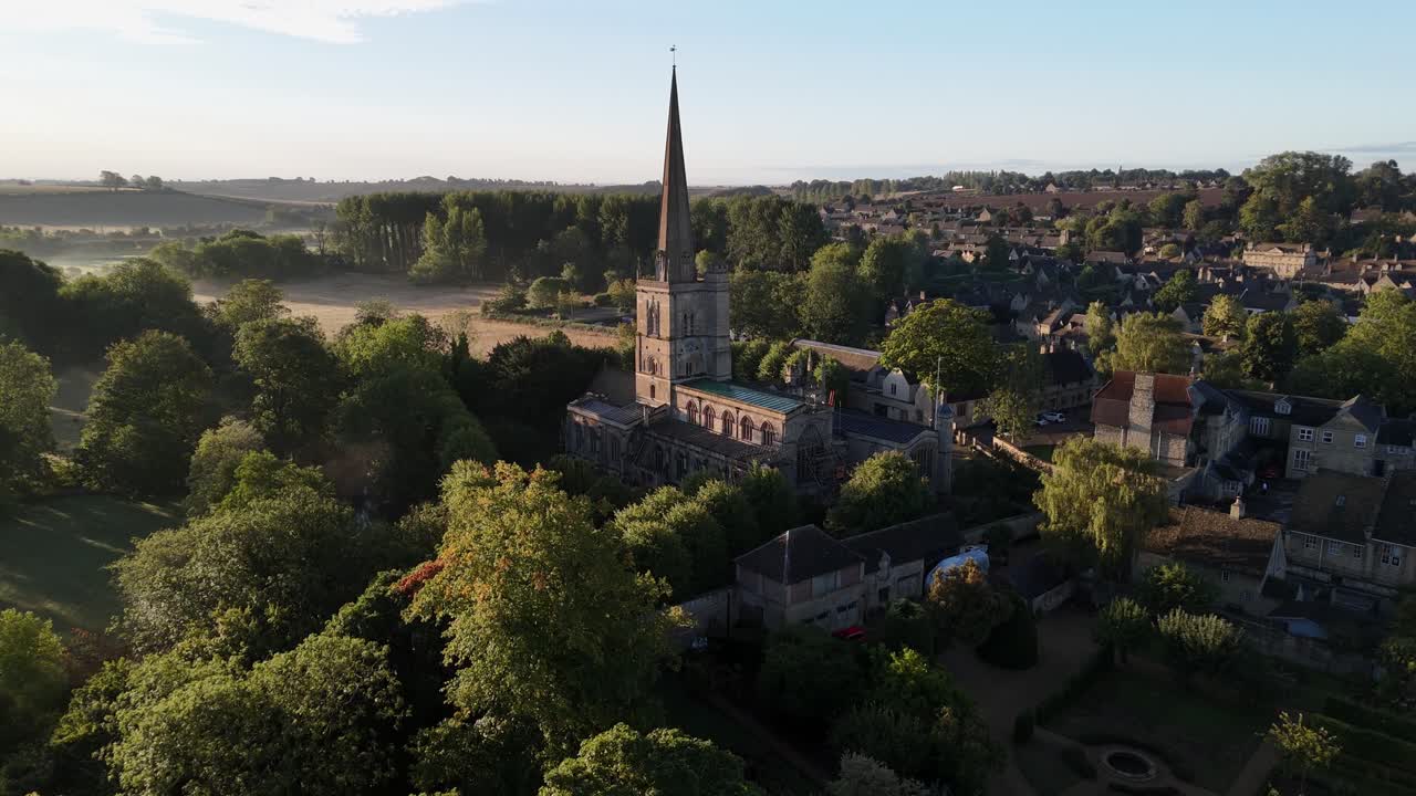 aerial drone aproach of the church in the village of Burford in the Cotswolds, bathed in the early morning sunlight