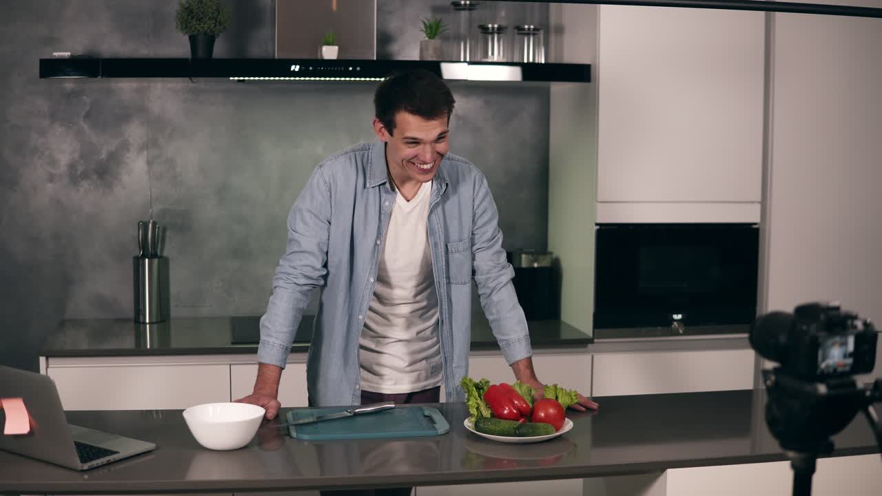 joven con ropa casual dirige un blog culinario y graba video en la cocina gris. video de rodaje del blog - da la bienvenida a su