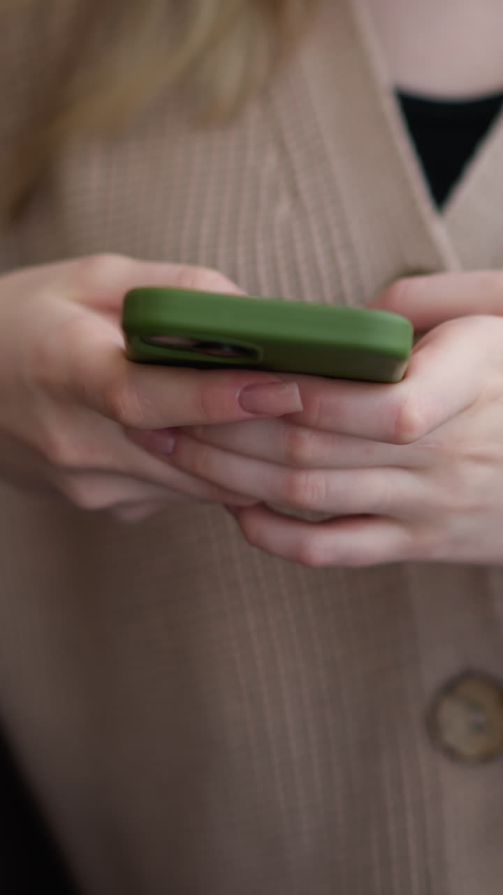 primer plano de una joven que opera un iphone con caja verde mientras está sentada en una mesa de madera, sus manos están enfocadas en la pantalla, mostrando atención a los detalles en un entorno relajado