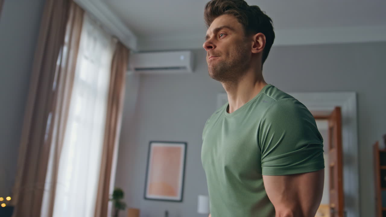 Muscular athlete training biceps at apartment close up. Man lifting dumbbells