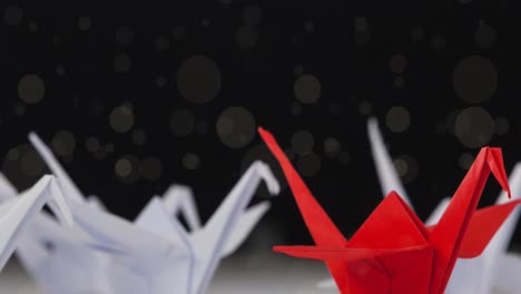 animación de manchas que caen sobre pájaros rojos y blancos de origami sobre fondo negro