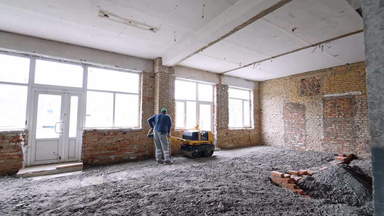 Male operates small steamroller to make floors in the spacious room. Using trench compactor equipment at the construction.