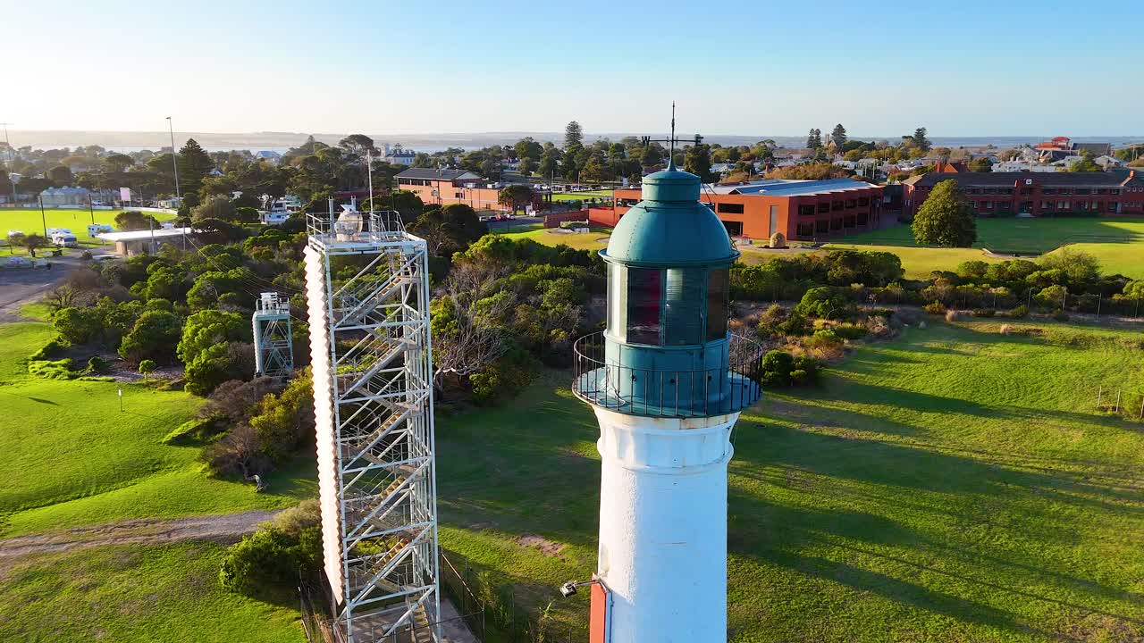 Drone footage captures the Queenscliff Lighthouse surrounded by lush greenery under clear skies, showcasing the serene landscape of Bellarine, Victoria