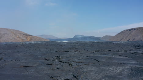 Aerial-drone-flying-low-above-vast-black-lava-lake-in-Fagradalsfjall,-Iceland,-forward,-day