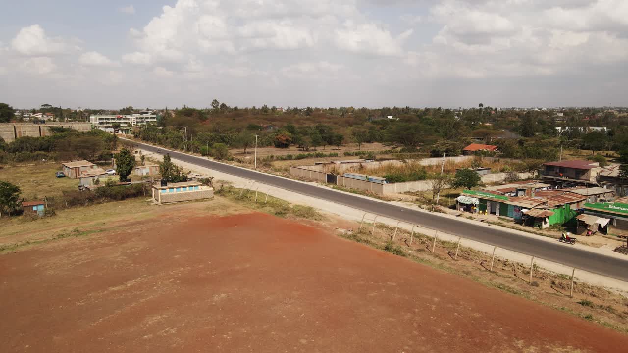 Ripresa aerea che sorvola una città rurale in Africa, mostrando un campo di terra rossa e una strada asfaltata