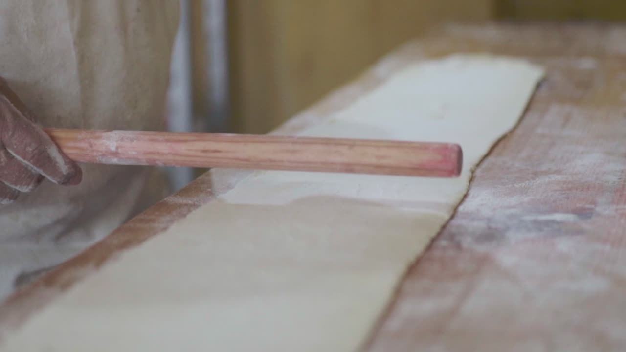 primer plano de un chef de pastelería rodando la masa con las manos usando un rodillo de madera en una superficie de trabajo