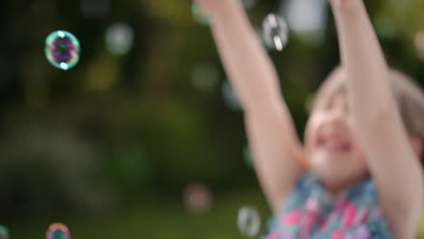 Fröhliches-Kleines-Mädchen,-Das-Spielerisch-Seifenblasen-Fängt,-Die-Mit-Einem-Niedlichen-Kind-Schwimmen,-Das-Spaß-Daran-Hat,-Blasen-Im-Sonnigen-Park-Zu-Platzen,-Unbeschwertes-Kindheitsspiel-4k