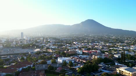 Drohnenaufnahme-Der-Stadt-San-Salvador-Mit-Bergen-Und-Vulkanen-In-Der-Ferne